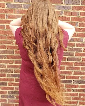 Long red hair with extensions, photographed against a brick wall.